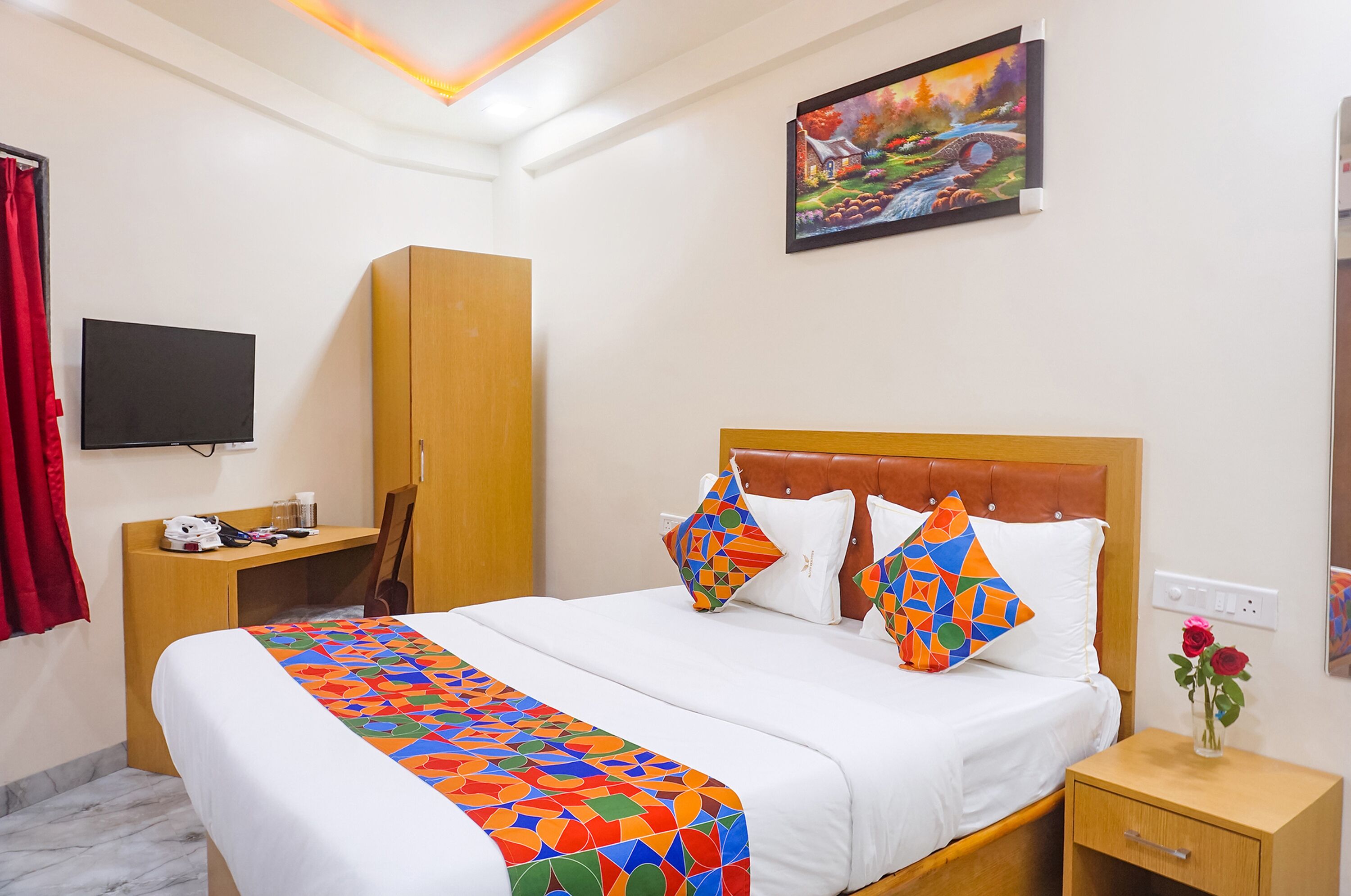 A hotel room with a large bed, a wooden wardrobe, a desk with a flat-screen TV, and a painting on the wall.