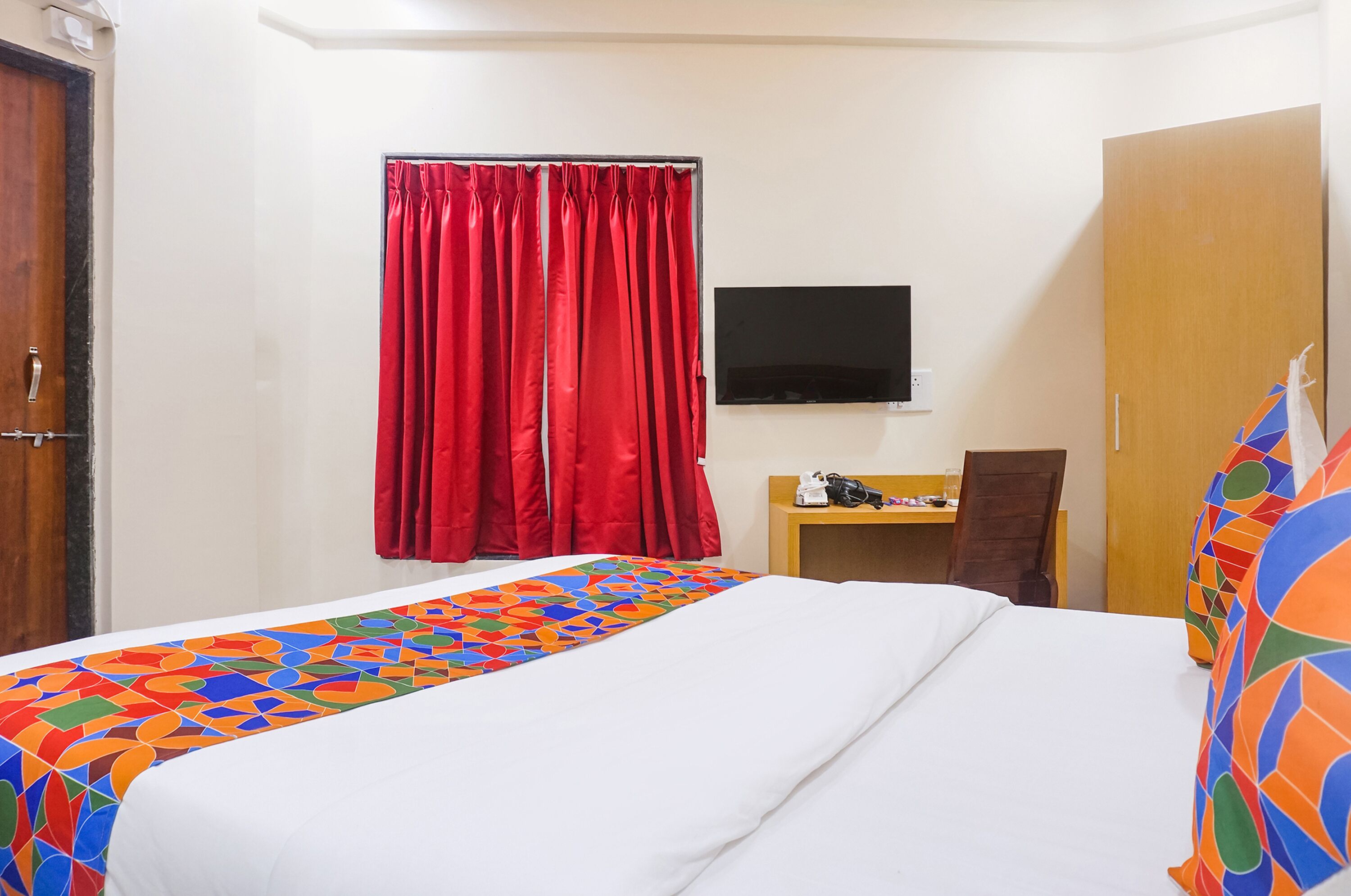 A hotel room with a bed, a desk, a chair, a TV, and a wardrobe.