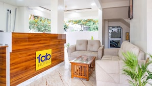 A hotel reception area with a wooden reception desk, a beige sofa, a glass coffee table, and a view of greenery outside. - Fabhotel Falcon Executive (Pune)