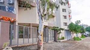 A residential building with a gated entrance, a tree in front, and a dirt road to the right. - Fabhotel Falcon Executive (Pune)