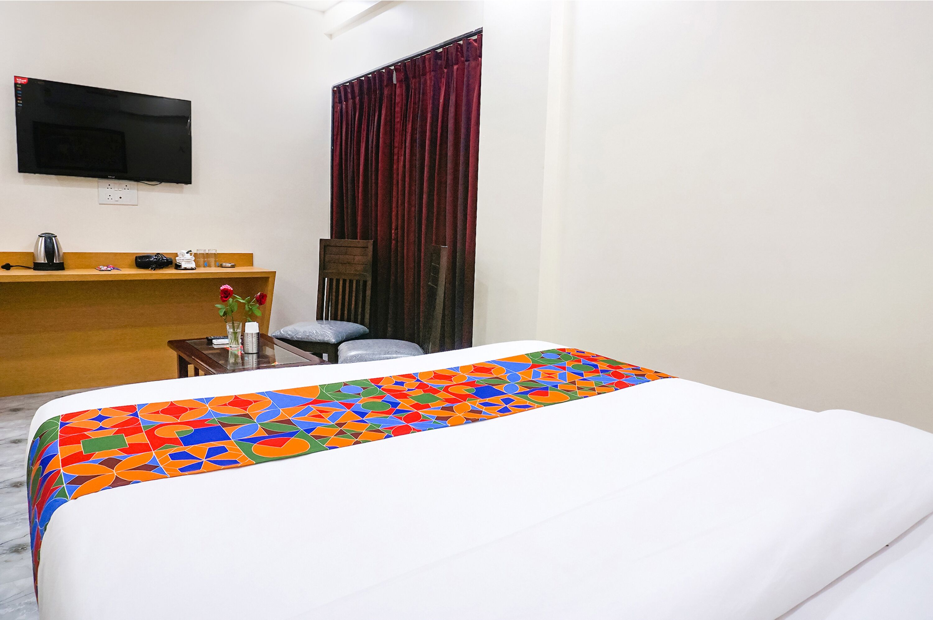 Habitación de hotel con cama, escritorio, silla, televisor montado en la pared y ventana con cortinas.