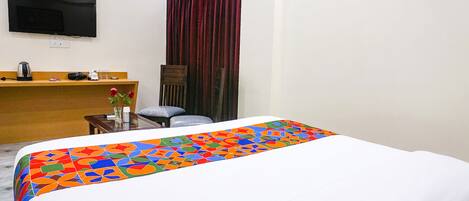 Habitación de hotel con cama, escritorio, silla, televisor montado en la pared y ventana con cortinas.
