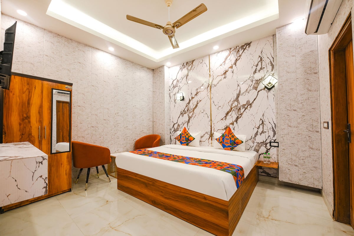 A modern bedroom with a marble-patterned wall, a wooden bed frame, a ceiling fan, and a small bedside table with a bottle.