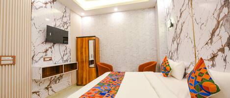 A hotel room with a bed, a TV mounted on the wall, a wooden wardrobe, and a ceiling fan.
