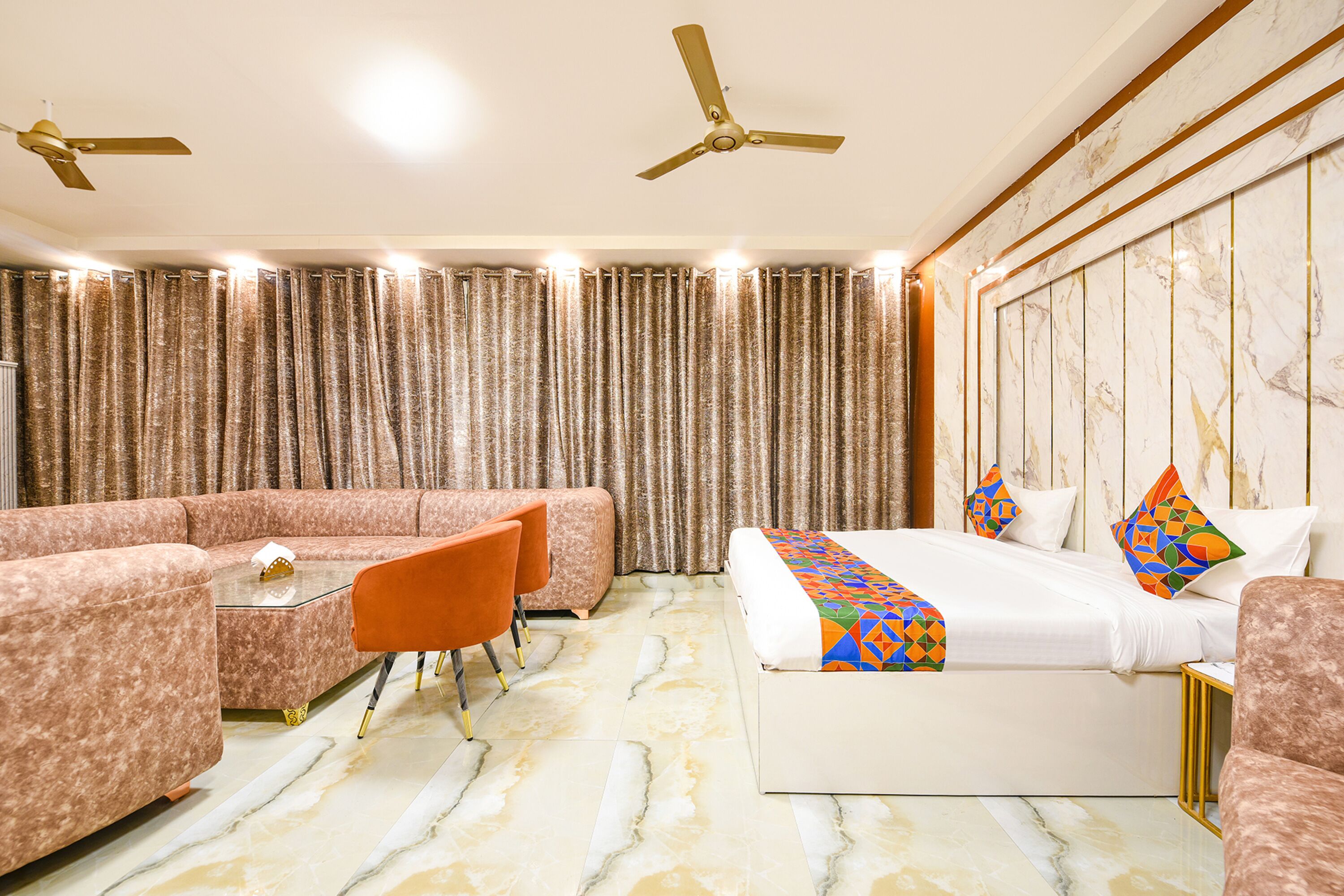 Une chambre d’hôtel avec un canapé, un lit agrémenté d’oreillers colorés, une petite table et un ventilateur de plafond.