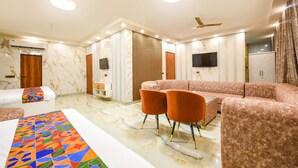 A modern hotel room with a large bed, two sofas, a dining table, and a TV. - Fabhotel Royal'S Paradise (Faridabad)