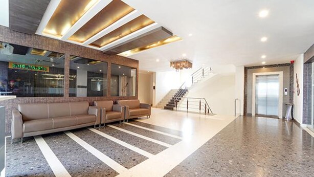 A modern lobby with a reception desk, seating area, and a staircase leading to an elevator. - Oriva Nestlay Rooms Ramnad (Ramanathapuram)