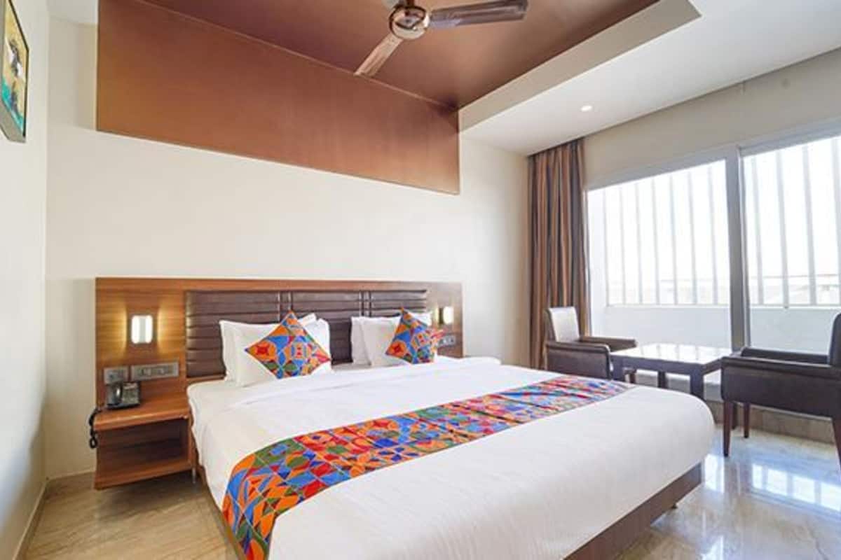 A hotel room with a large bed, a wooden headboard, a nightstand, a desk, and a chair.