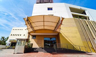 Um edifício moderno com marquise de entrada curva, escadaria visível que leva à entrada e céu claro.