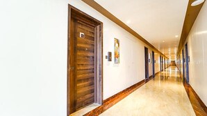A long, well-lit hallway with wooden doors and a marble floor. - Oriva Nestlay Rooms Ramnad (Ramanathapuram)
