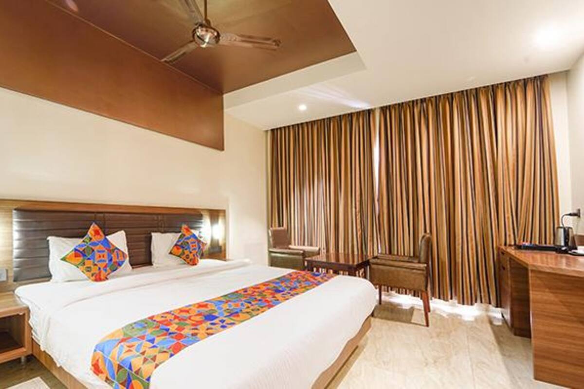 A hotel room with a large bed, a desk, a chair, and a ceiling fan.