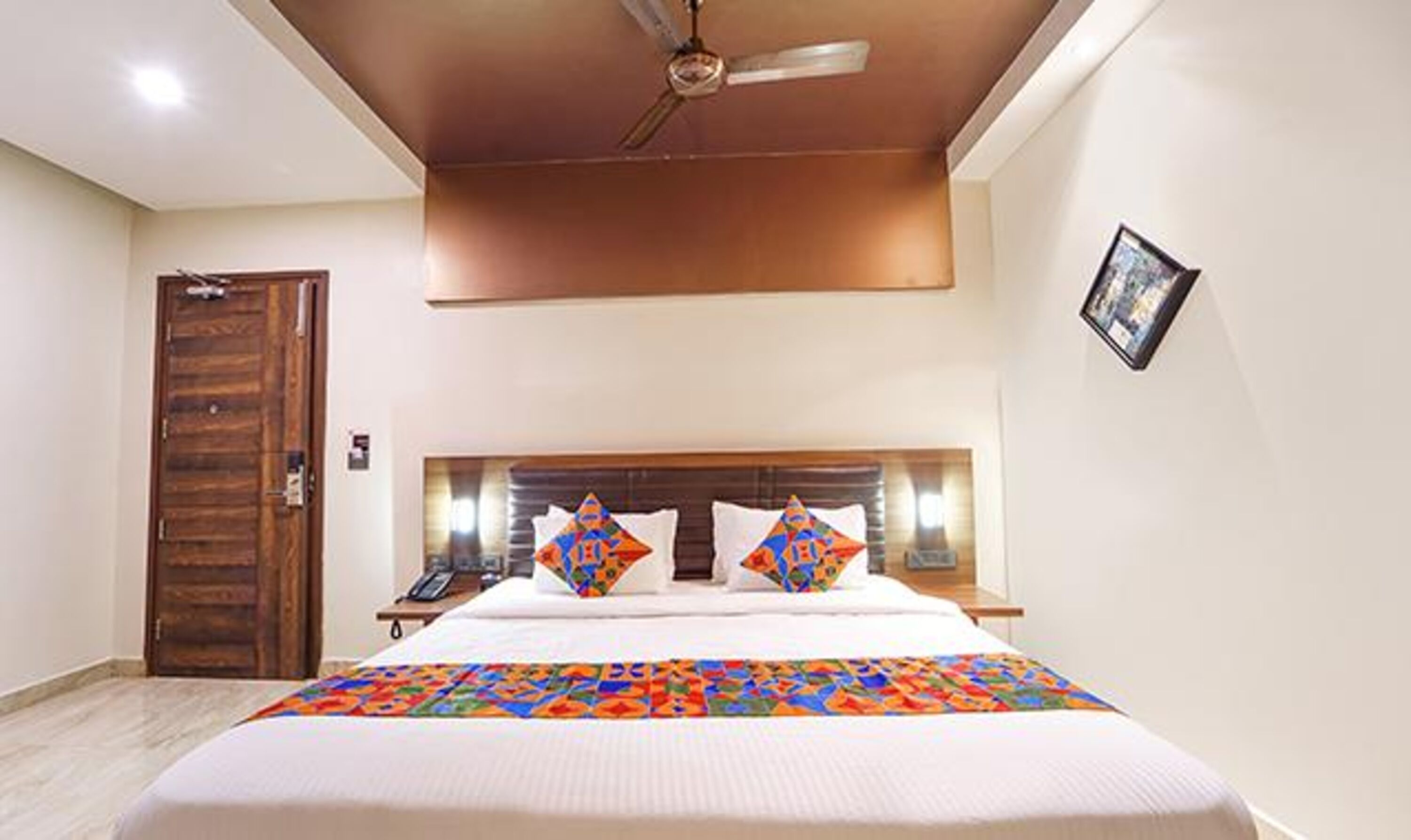 Quarto de hotel com cama, ventoinha no teto, porta de madeira e mesa de cabeceira com telefone.