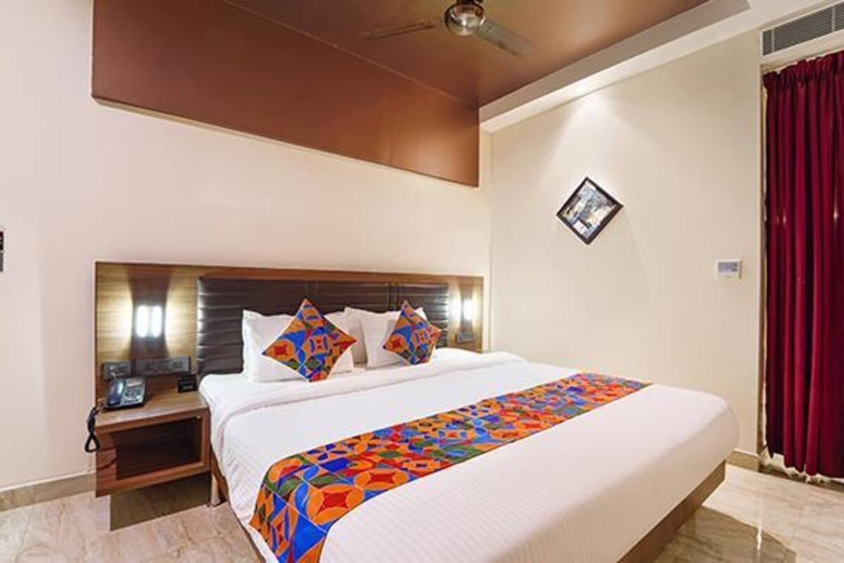A hotel room with a large bed, a wooden headboard, a bedside table with a phone, and a red curtain.