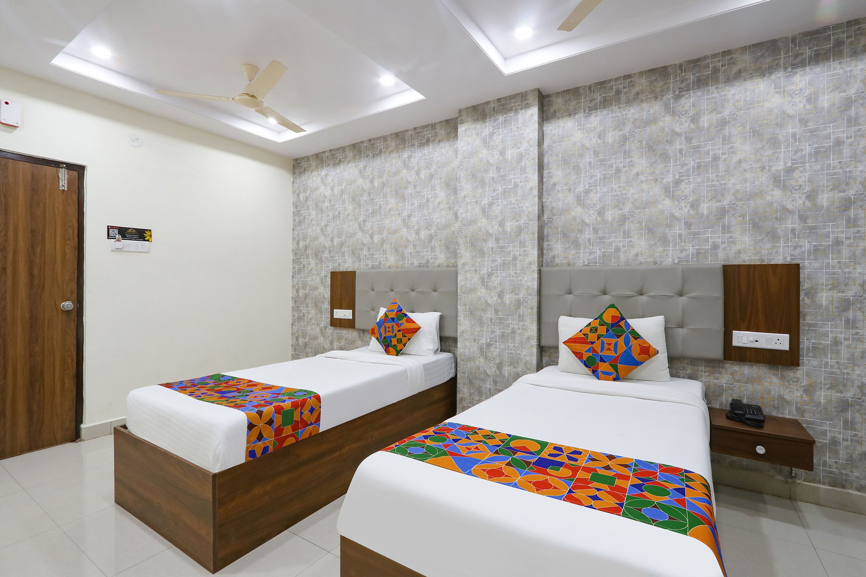 A hotel room with two beds, a wooden wardrobe, a nightstand, a ceiling fan, and a textured wall.