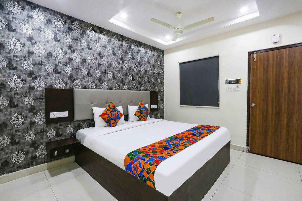A bedroom with a bed, a ceiling fan, a dark wooden door, and a patterned wall.