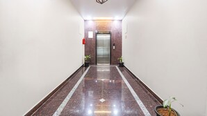 A hallway with a polished marble floor, a modern elevator, and potted plants.