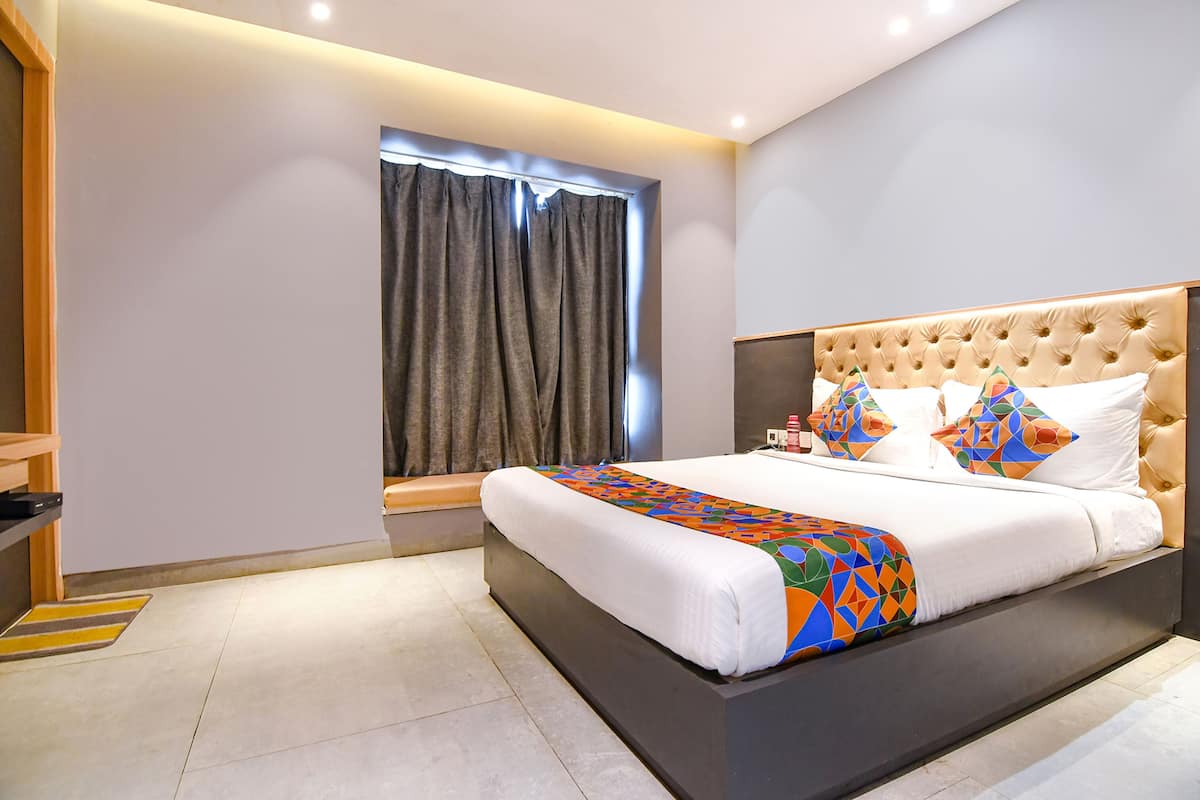 Moderni hotellihuone, jossa on suuri sänky, ikkuna verhoilla ja yöpöytä.