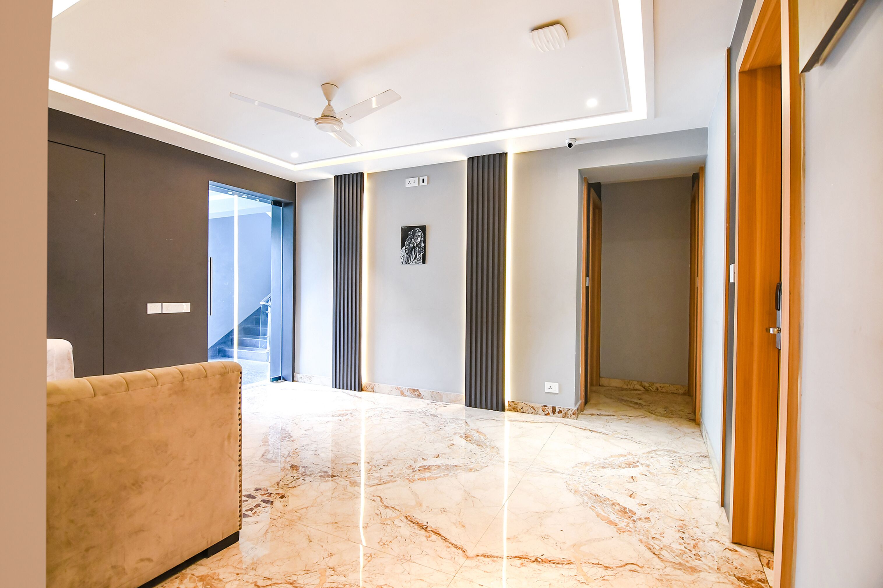 A modern interior with a marble floor, a sofa, a ceiling fan, and a staircase leading to an upper level.