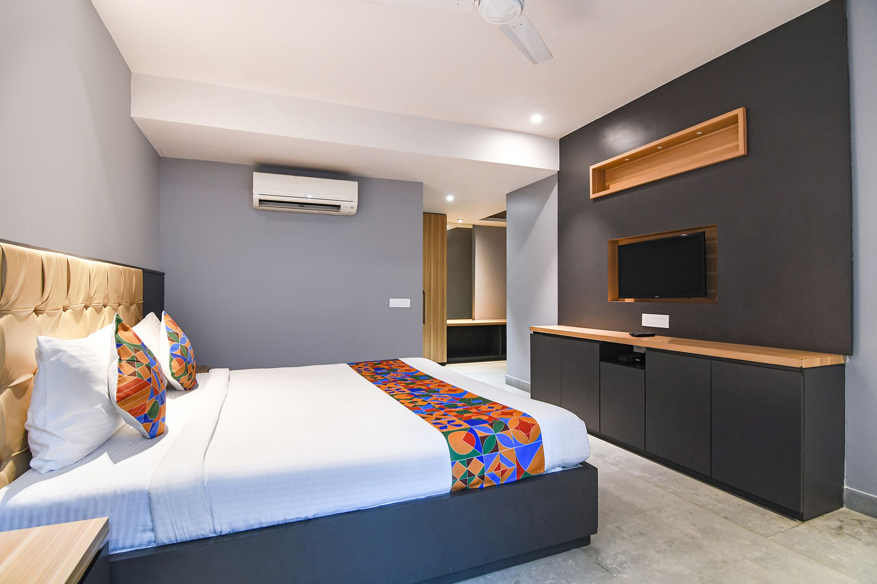 A modern hotel room with a large bed, a built-in desk, a flat-screen TV, and an air conditioning unit.