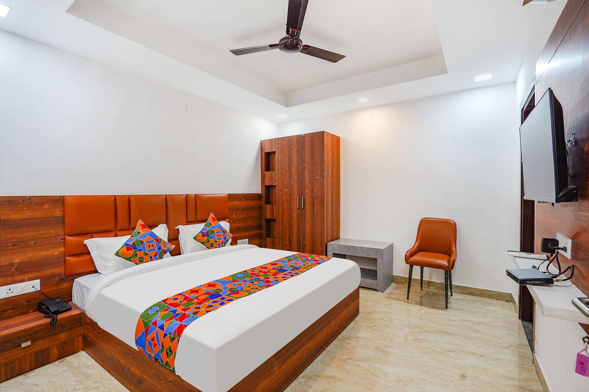 A modern hotel room with a large bed, wooden headboard, a desk with a chair, a wardrobe, and a ceiling fan.