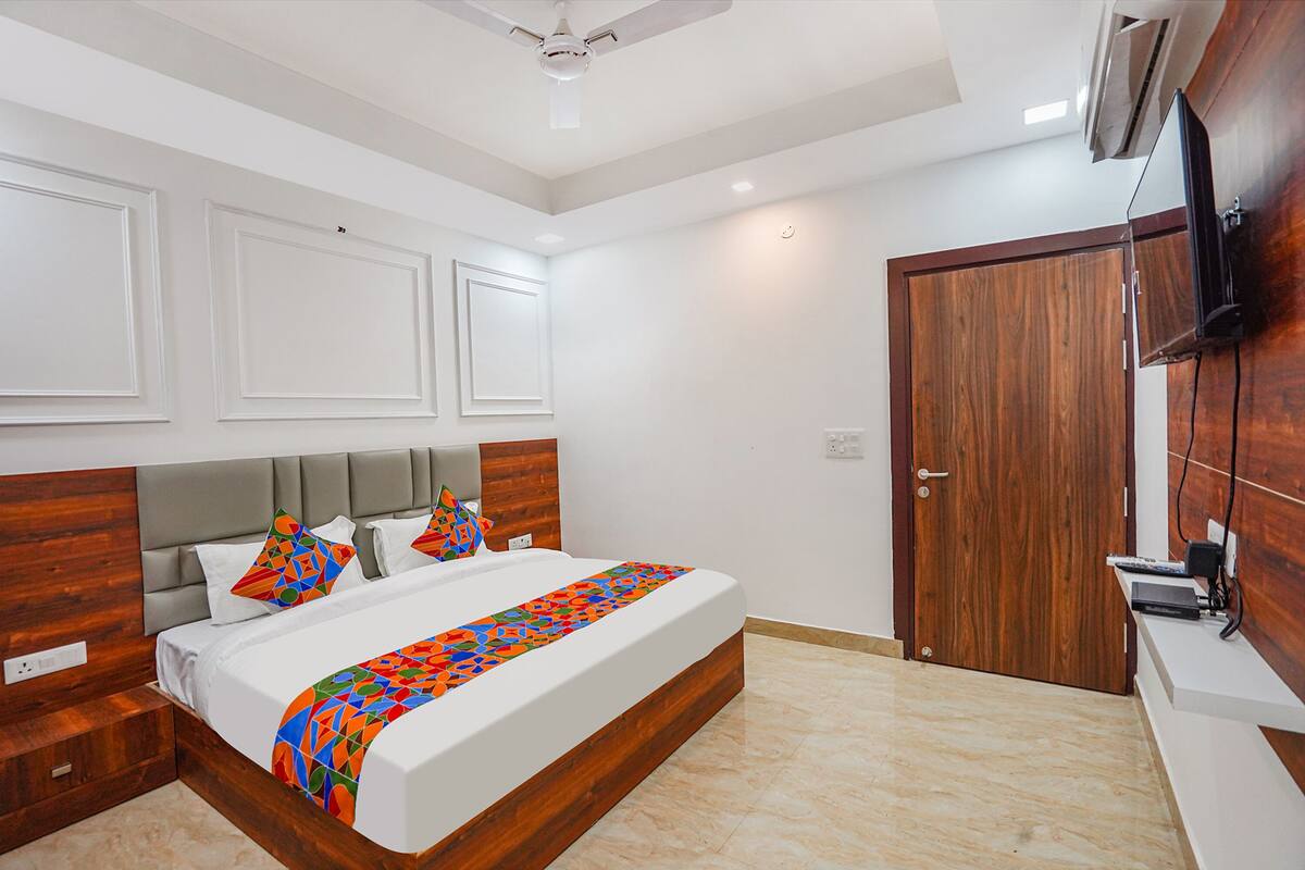 A bedroom with a bed, a wooden headboard, a TV mounted on the wall, and a door.