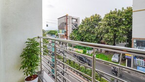 A balcony with a potted plant, a metal railing, and a view of a busy street with vehicles and buildings. - Fabhotel Willow Tree (Bengaluru)