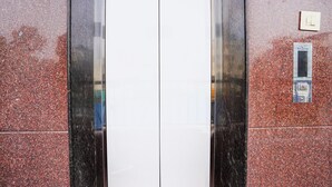 An elevator with a metallic interior and a red speckled exterior wall. - Fabhotel Willow Tree (Bengaluru)