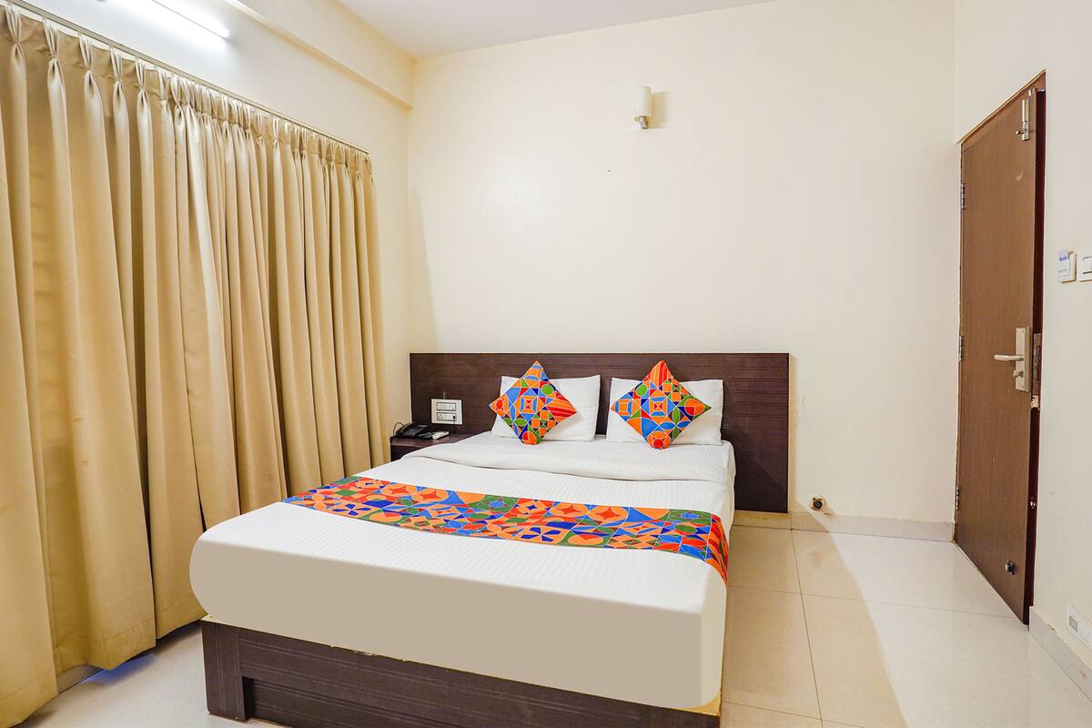 A neatly made bed with a colorful bedspread and two decorative pillows, a bedside table with a phone, and a door to the right.