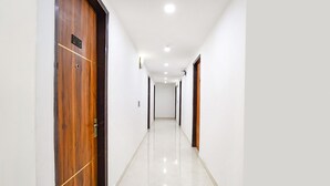 A long, narrow hallway with wooden doors on both sides and a shiny, reflective floor. - Fabhotel Prime Emporio Villa By Sbg (Ghaziabad)