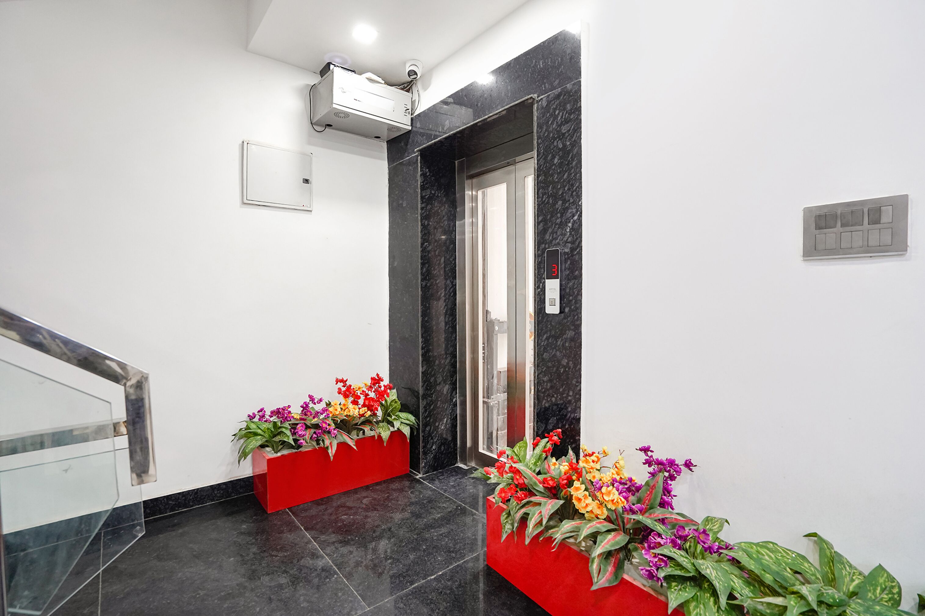 Um elevador moderno com visor digital, um cachepot vermelho com flores e uma parede de mármore.