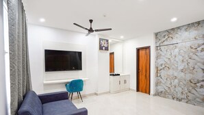 A modern living room with a flat-screen TV, a blue sofa, a ceiling fan, and a marble-patterned wall. - Fabhotel Prime Emporio Villa By Sbg (Ghaziabad)