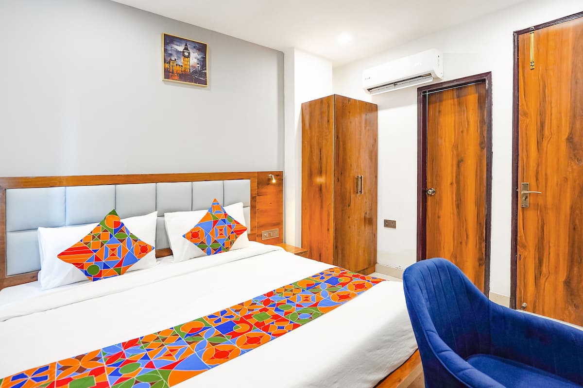 Une chambre d’hôtel avec un lit, une chaise bleue, une armoire en bois et un tableau représentant un paysage urbain.
