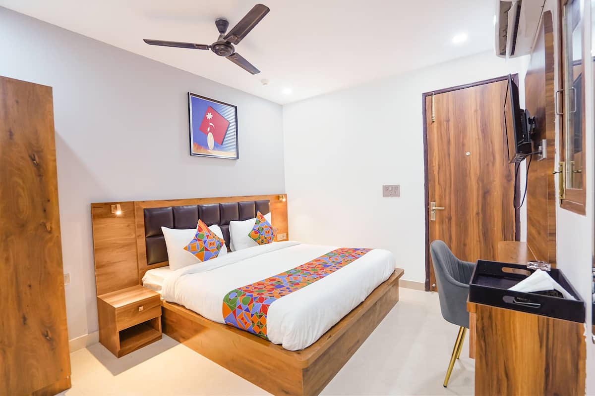 Une chambre à coucher avec un lit en bois, un bureau, une chaise, un ventilateur de plafond et un téléviseur fixé au mur.