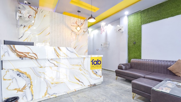 A hotel reception area with a marble reception desk, a brown leather sofa, and a green wall accent. - Fabhotel Madhav (Mathura)