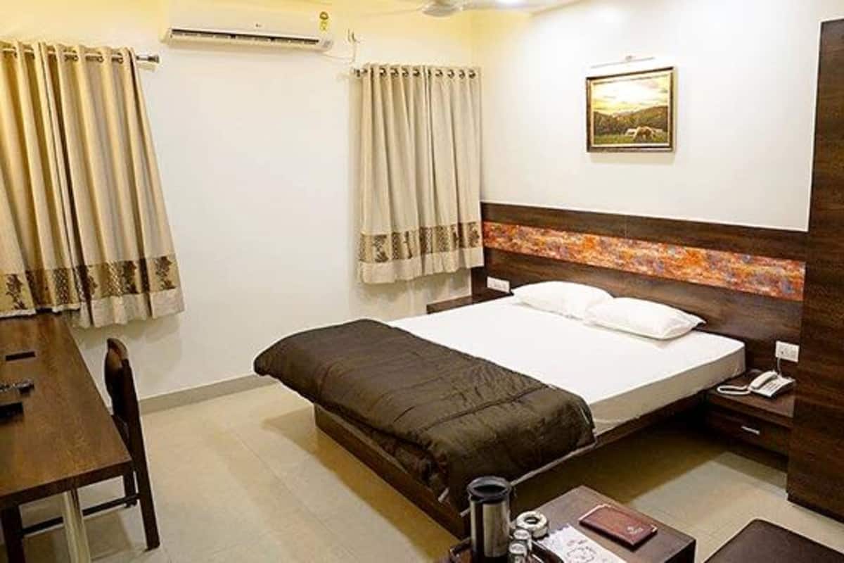 A hotel room with a bed, a desk, a chair, a wardrobe, and a painting on the wall.