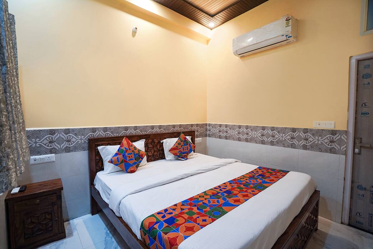 A neatly made bed with a colorful geometric-patterned blanket, a wooden headboard, and a wall-mounted air conditioner.