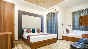 A modern hotel room with a wooden bed, a sofa bed, a ceiling fan, and a small seating area with stools. - Fabhotel Vasudha (Mathura)