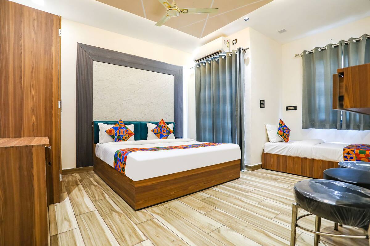 A modern hotel room with a wooden bed, a sofa bed, a ceiling fan, and a small seating area with stools.