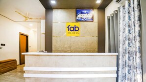 A reception desk with a 'fab hotels' sign, a framed picture above, and a curtain with a floral pattern. - Fabhotel Vasudha (Mathura)