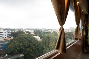 A view from a window with curtains tied back, overlooking a cityscape with buildings and trees. - FabHotel Royal Sterling (Bengaluru)