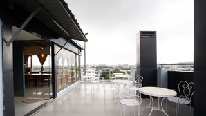 A rooftop terrace with white metal tables and chairs, a glass door entrance, and a view of the cityscape. - FabHotel Royal Sterling (Bengaluru)