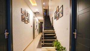 A hotel hallway with a staircase, framed pictures on the walls, and a sign indicating the rooms. - FabHotel Royal Sterling (Bengaluru)