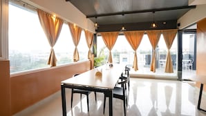 A spacious room with a long table and chairs, large windows with curtains, and a city view. - FabHotel Royal Sterling (Bengaluru)