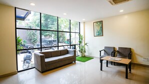 A modern waiting area with a sofa, chairs, a table, and large windows offering a view of the street. - FabHotel Royal Sterling (Bengaluru)