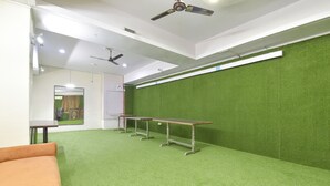 A room with green artificial grass flooring, a long table, a sofa, and ceiling fans. - Fabhotel Rajwada Palace (Jaipur)