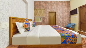 A hotel room with a bed, a chair, a door, and a wall-mounted TV. - Fabhotel Rajwada Palace (Jaipur)