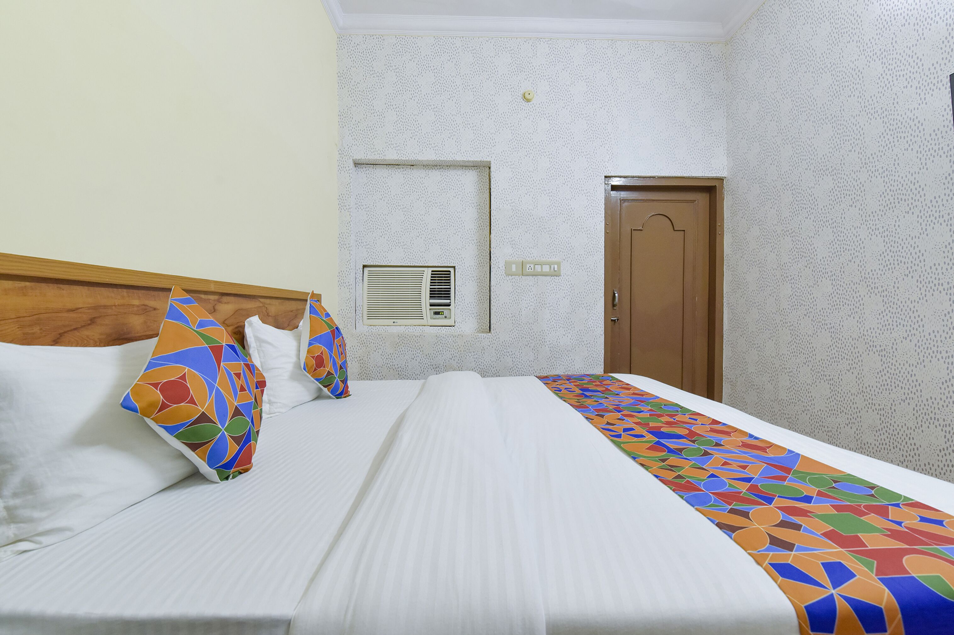 Une chambre d’hôtel avec un lit, une tête de lit en bois, un mur à motifs, une porte et un climatiseur fixé au mur.