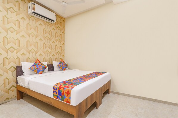 A neatly made bed with a colorful geometric-patterned bedspread and pillows, a wooden headboard, and a wall-mounted air conditioner.