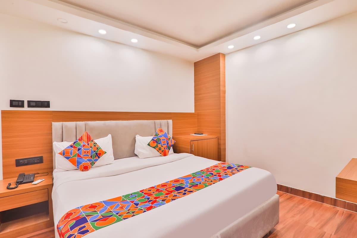 A modern hotel room with a large bed, a wooden headboard, a bedside table with a phone, and a nightstand.