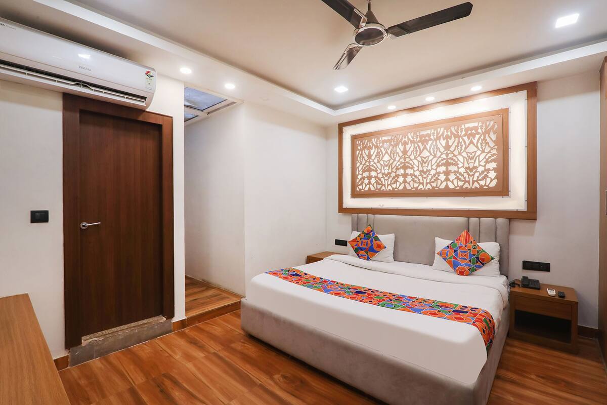 A bedroom with a bed, a ceiling fan, an air conditioning unit, a wooden door, and a decorative wall panel.